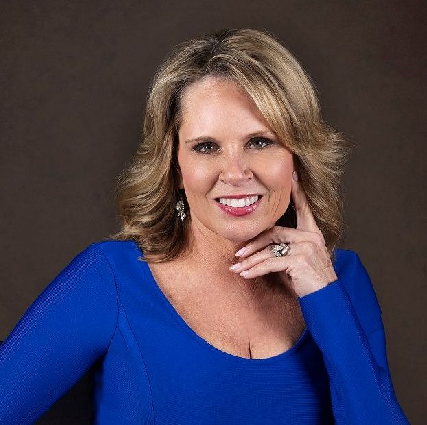 A woman in a blue dress is smiling and holding her hand to her face.