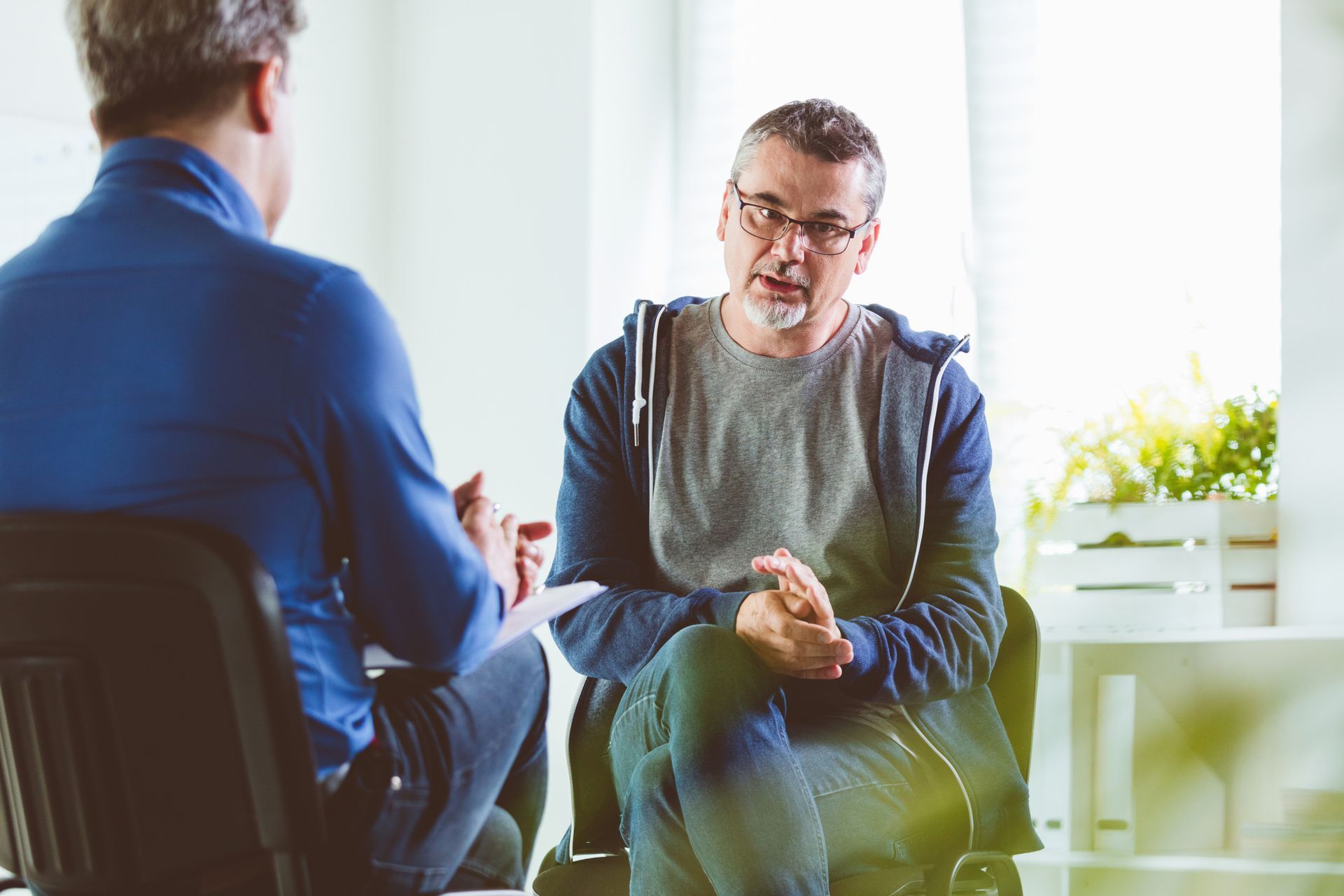 A man is sitting in a chair talking to another man.