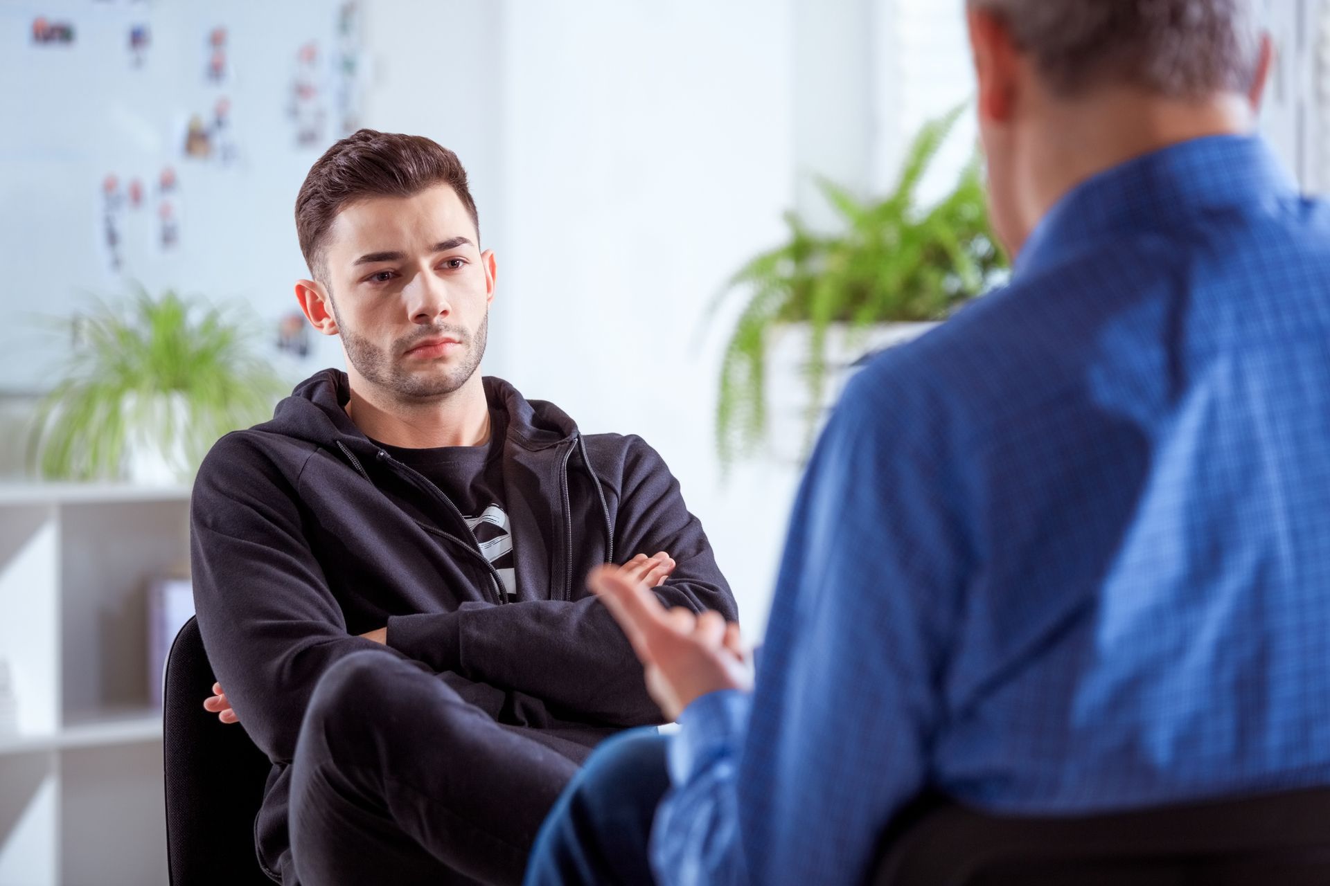 A man is sitting in a chair talking to another man.