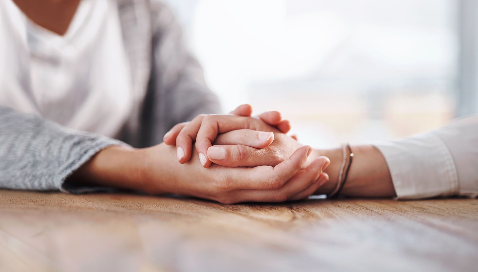A woman is holding another woman's hand while sitting at a table.