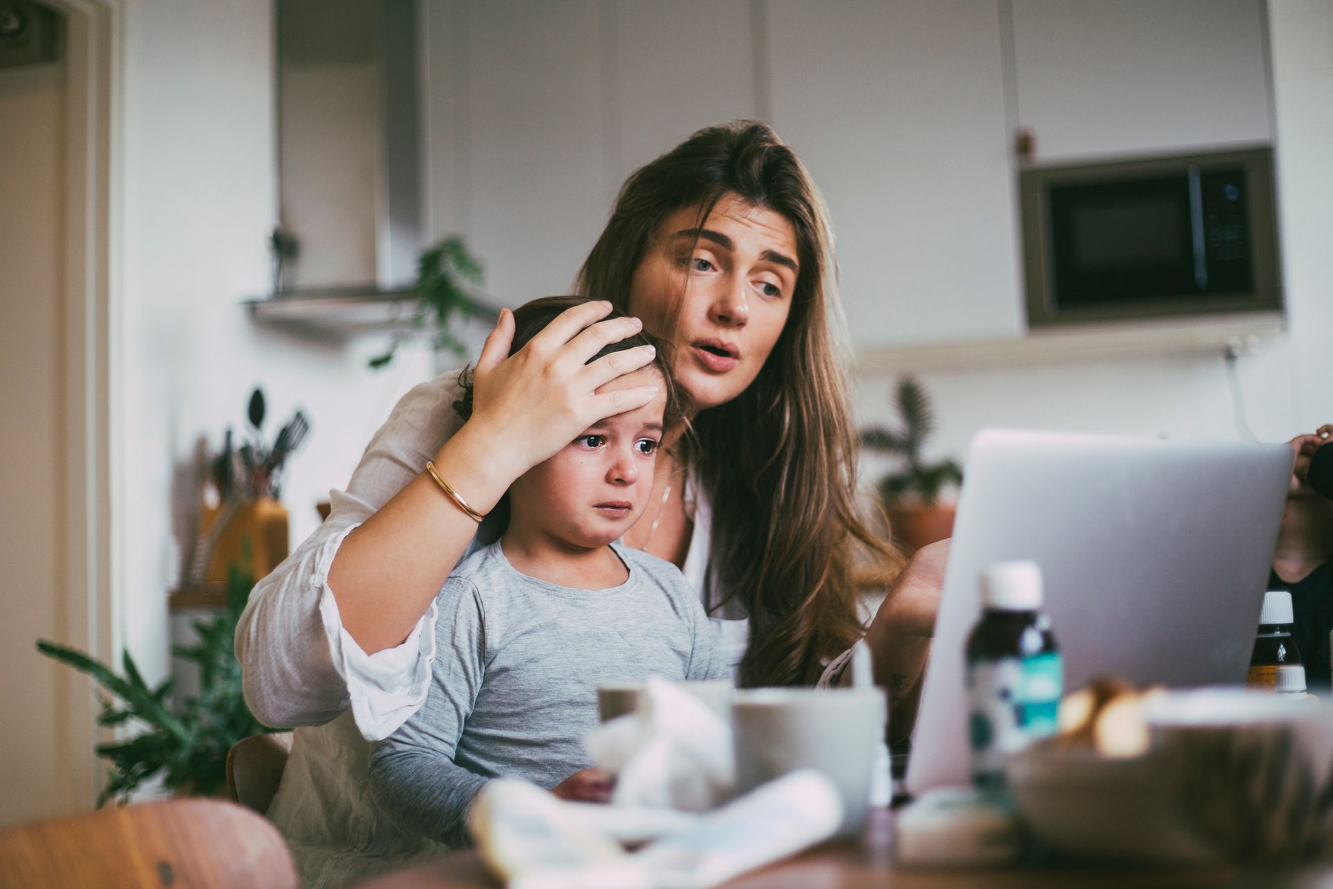 A woman is holding a child while looking at a laptop.