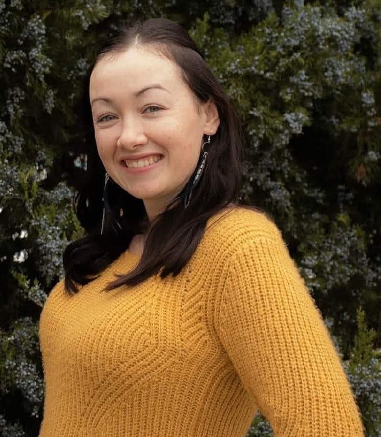 Woman in yellow sweater smiles outdoors.
