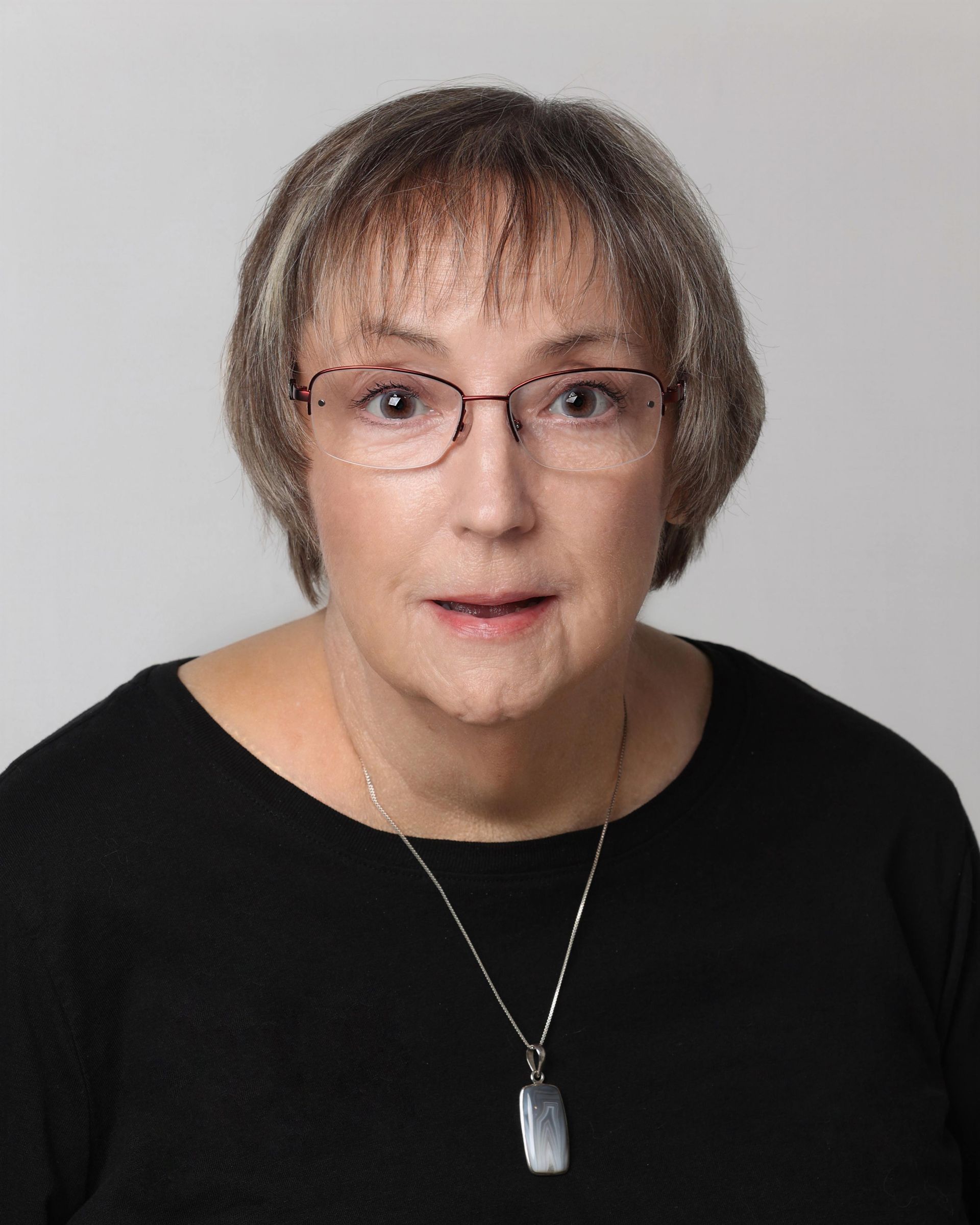Woman with glasses, short gray hair, and black shirt, looking directly at the camera.