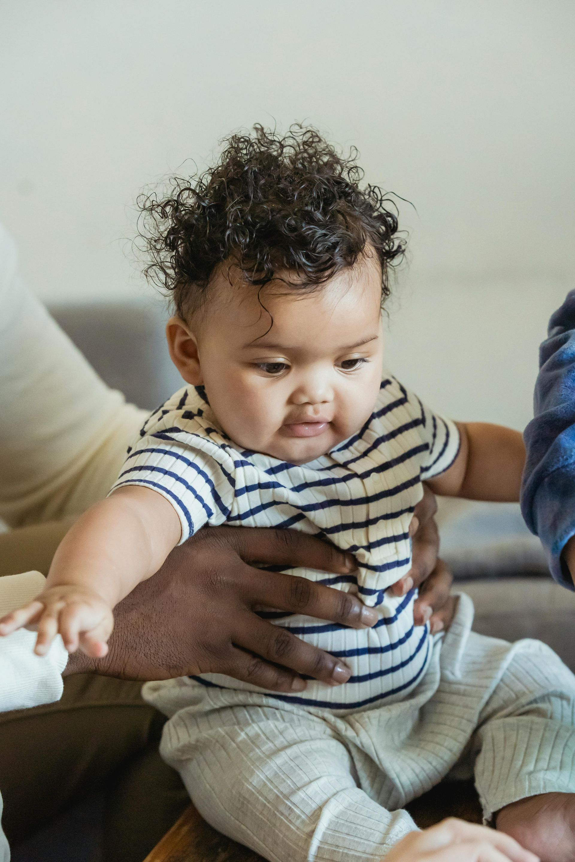 Baby in striped shirt reaching out while being supported on a couch
