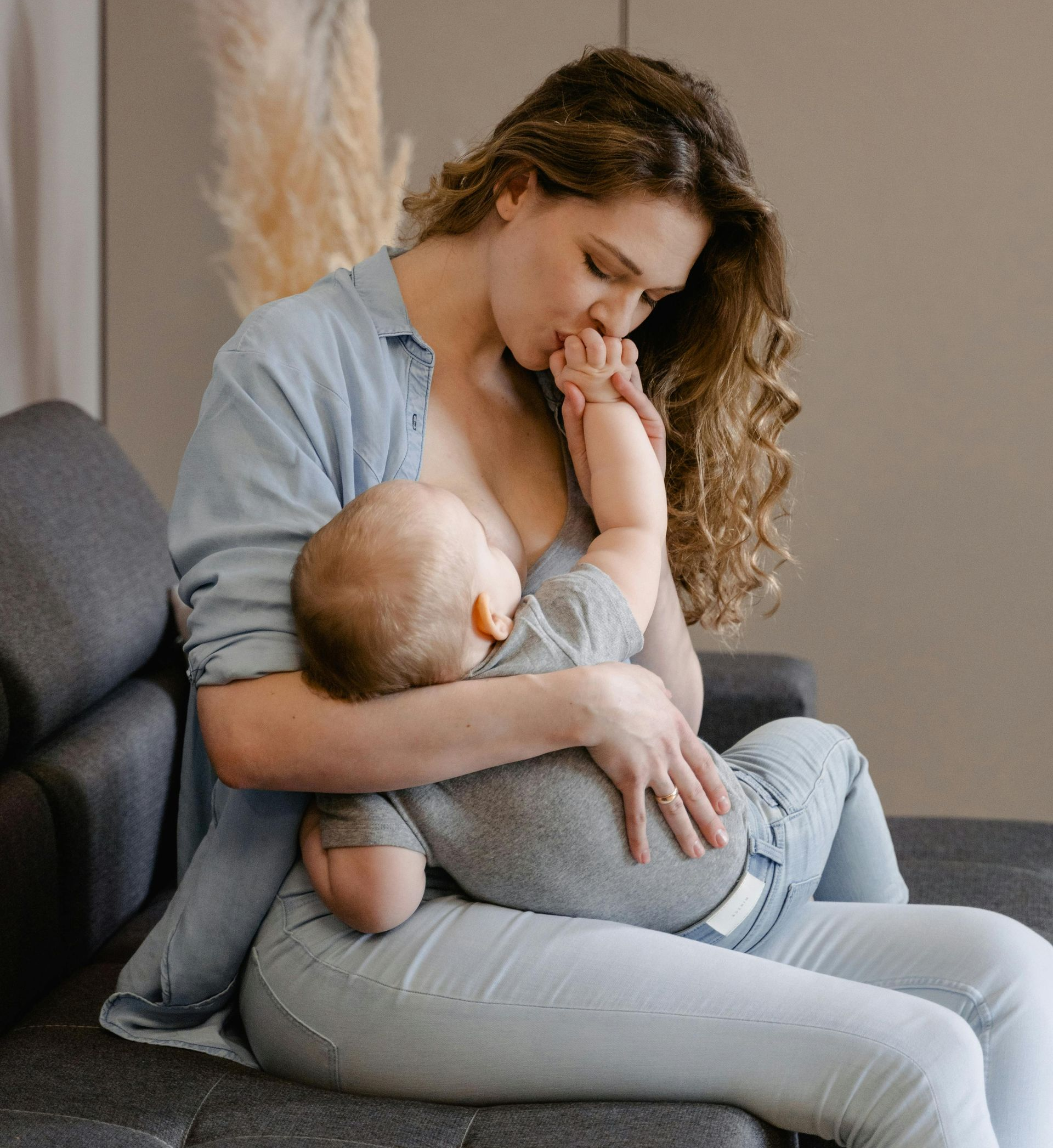 Woman sitting on a couch, gently holding and looking at a sleeping baby.