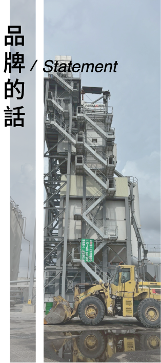 在陰沉的天空下,一輛黃色前裝式裝載機停在一座高大的灰色工業混凝土或瀝青攪拌站前。
