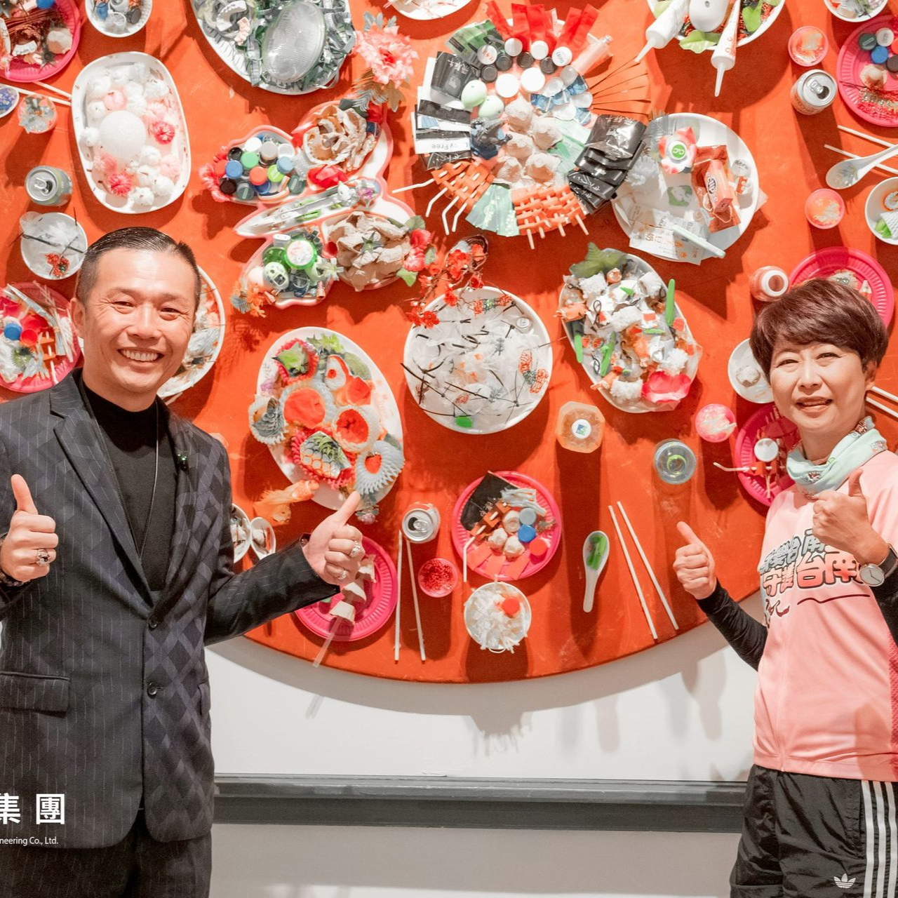 兩個人面帶微笑,豎起大拇指站在一個圓形橙色展示架前,展示架上擺放著各種白色陶瓷盤。