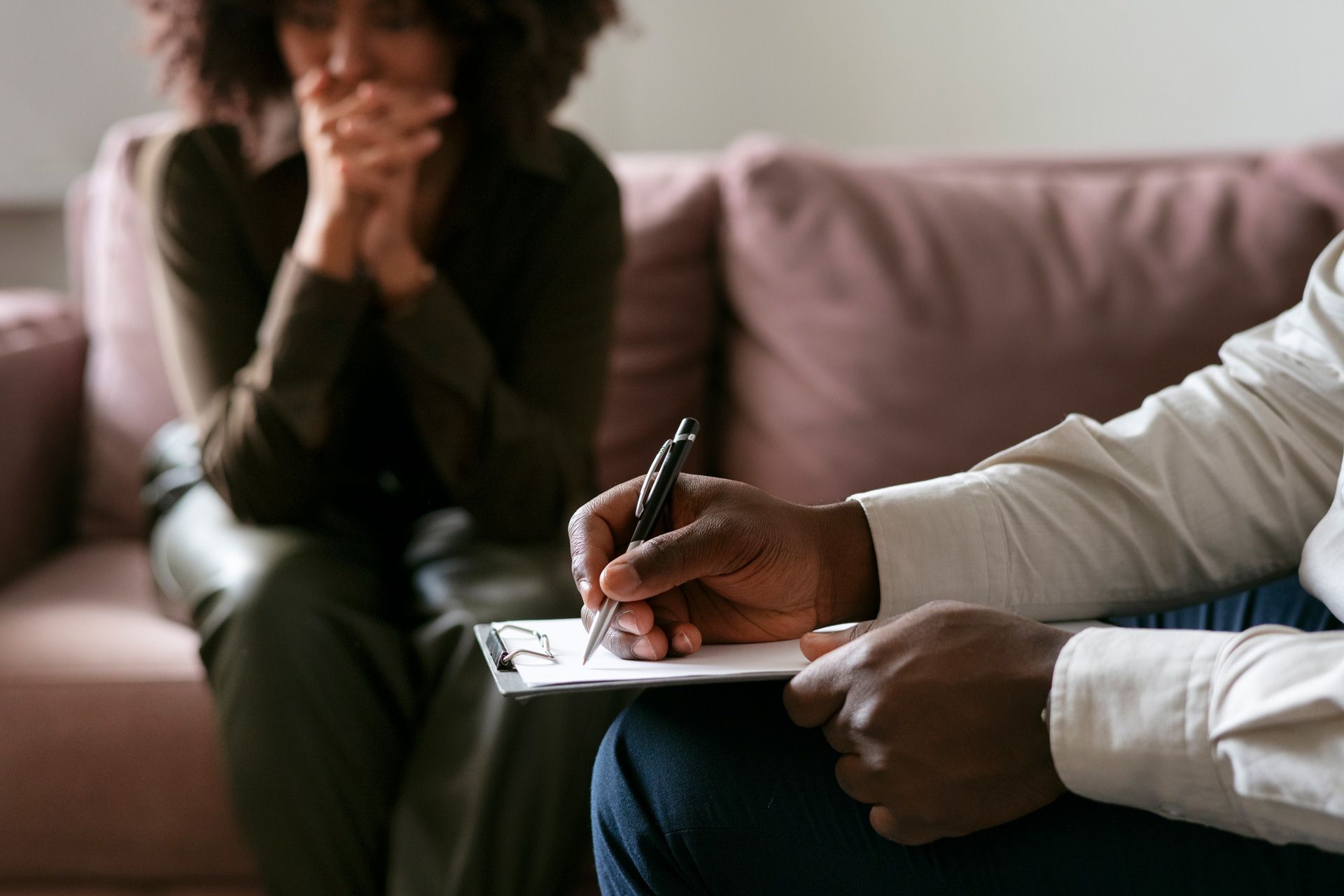 A man is writing on a clipboard while a woman sits on a couch.