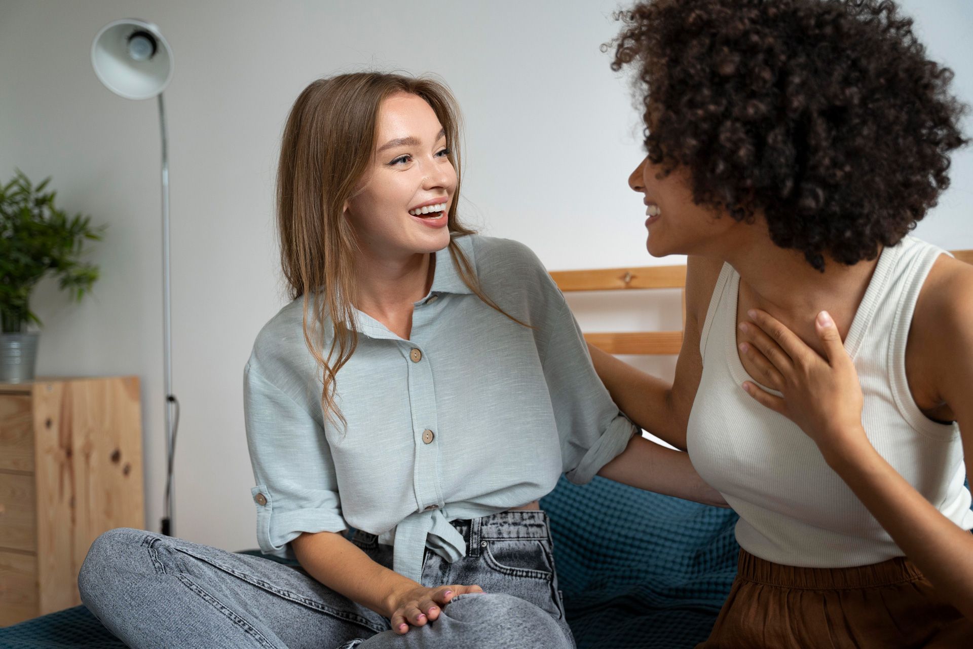 Two women are sitting on a bed talking to each other.