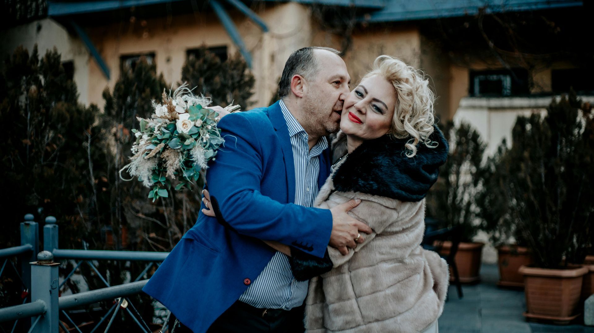 A man is kissing a woman on the cheek while holding a bouquet of flowers.