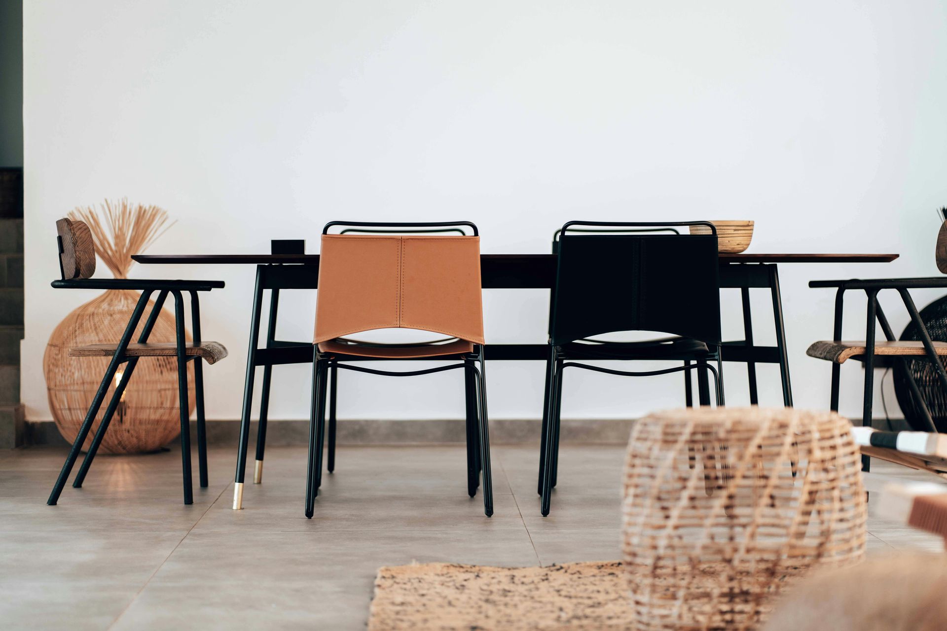 Minimal dining room with a black table, mixed chairs, and woven decor against a white wall