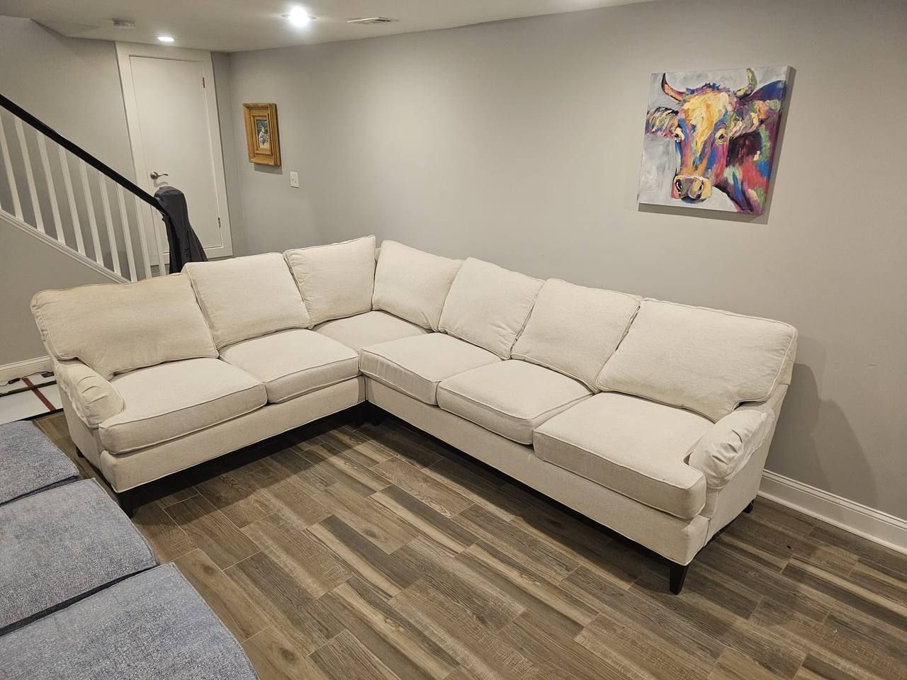 Beige sectional sofa in a room with hardwood floors and art on the wall.