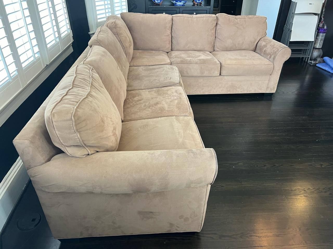 Beige sectional sofa in a room with a recliner and windows.