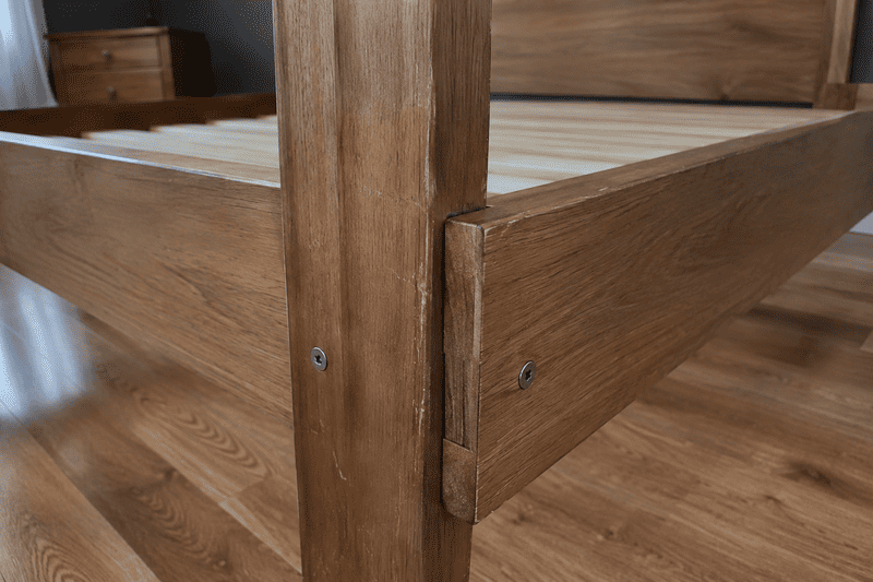 Close-up of a wooden bed frame corner with a jointed support and slatted base.