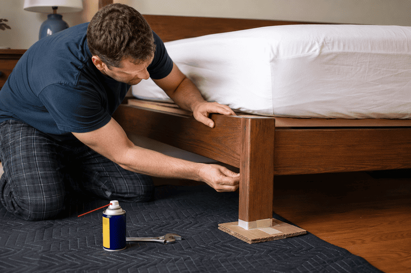 Man assembling a wooden bed frame beside a mattress with tools on the floor