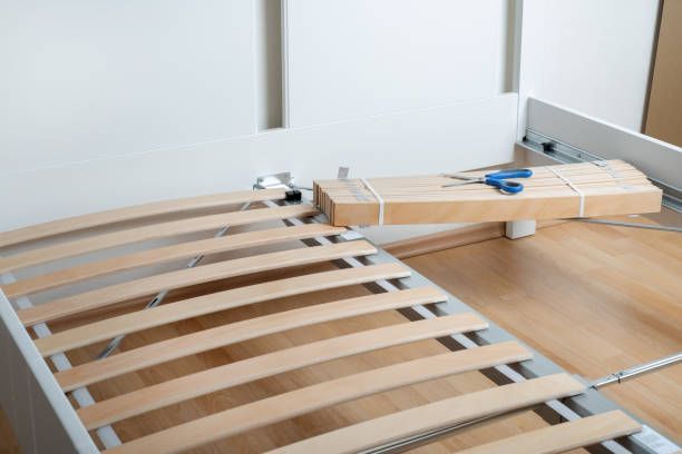 Partially assembled wooden bed frame with slats and tools in a bright bedroom