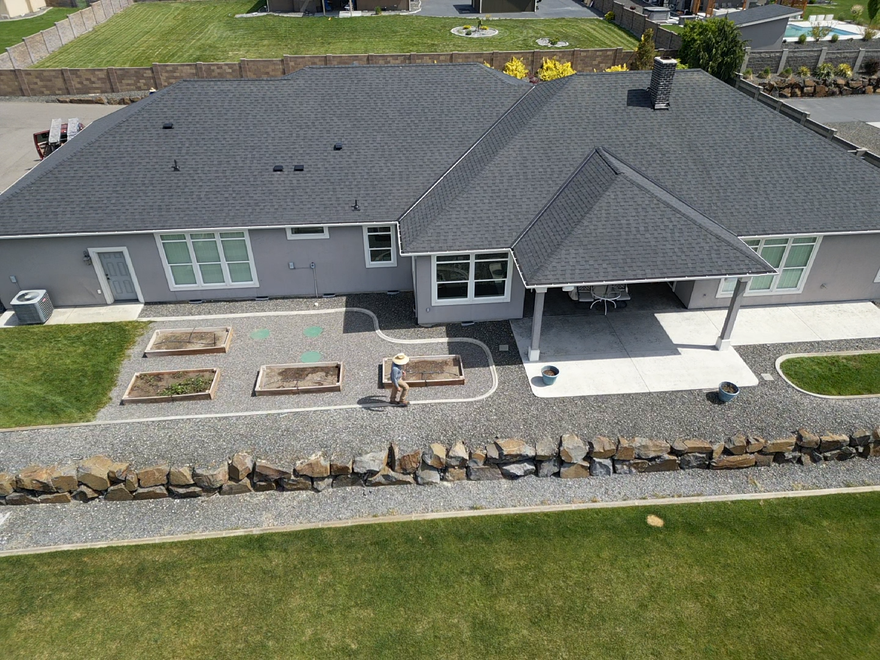 Gray shingle roof with several vents. A grassy yard and vineyard are in the background.