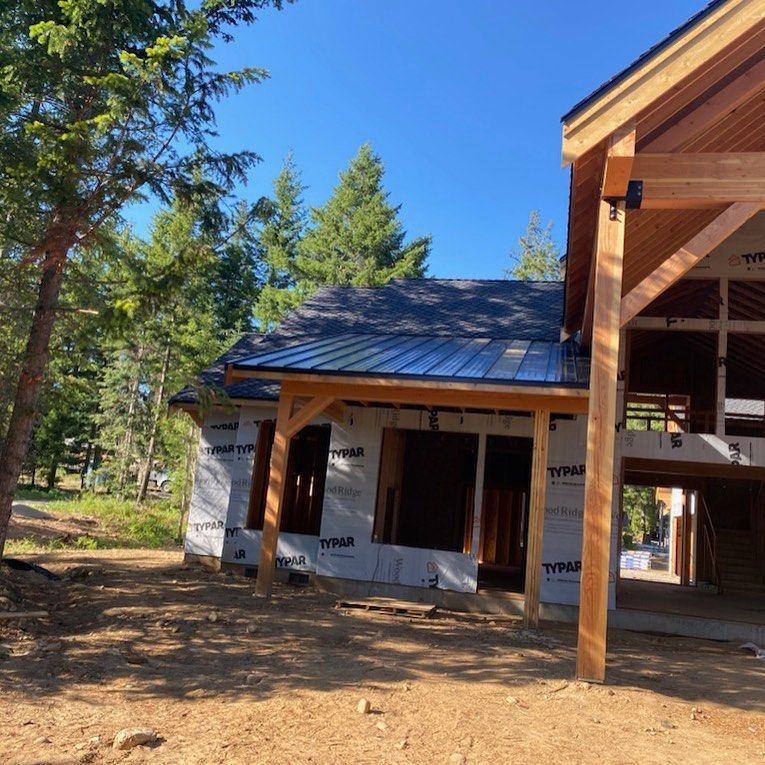 Exterior view of a house under construction with a black metal roof and exposed wooden beams.