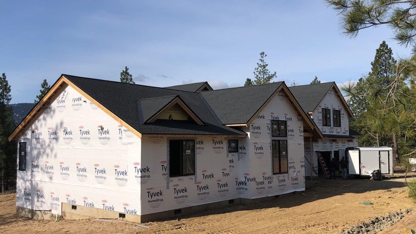 House under construction with black roof and white wrap.