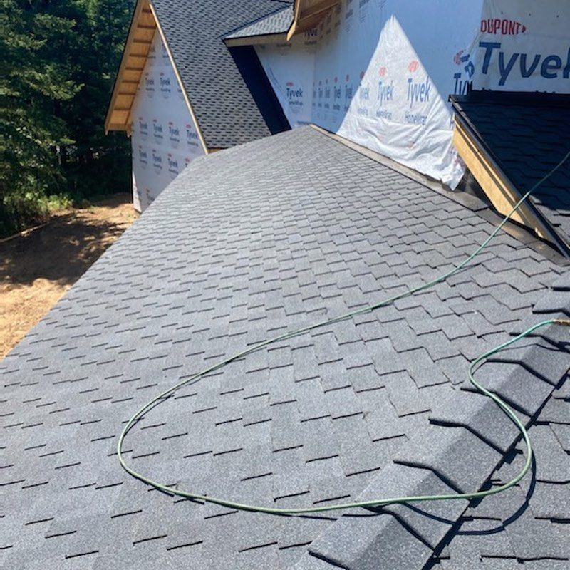 Newly shingled roof with dark gray asphalt shingles, green electrical cord. Construction site, outdoor, daylight.