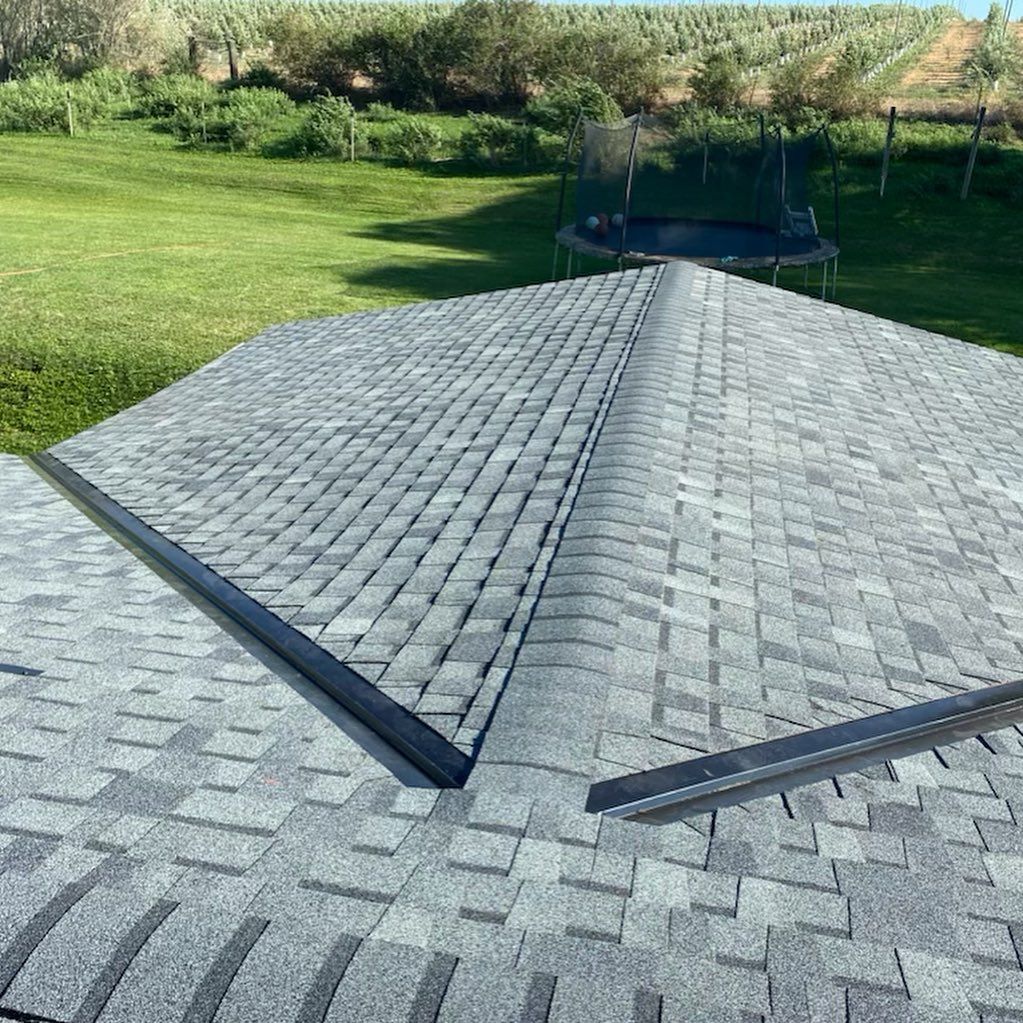 Gray asphalt shingle roof with black metal trim. Green yard and trampoline in background.
