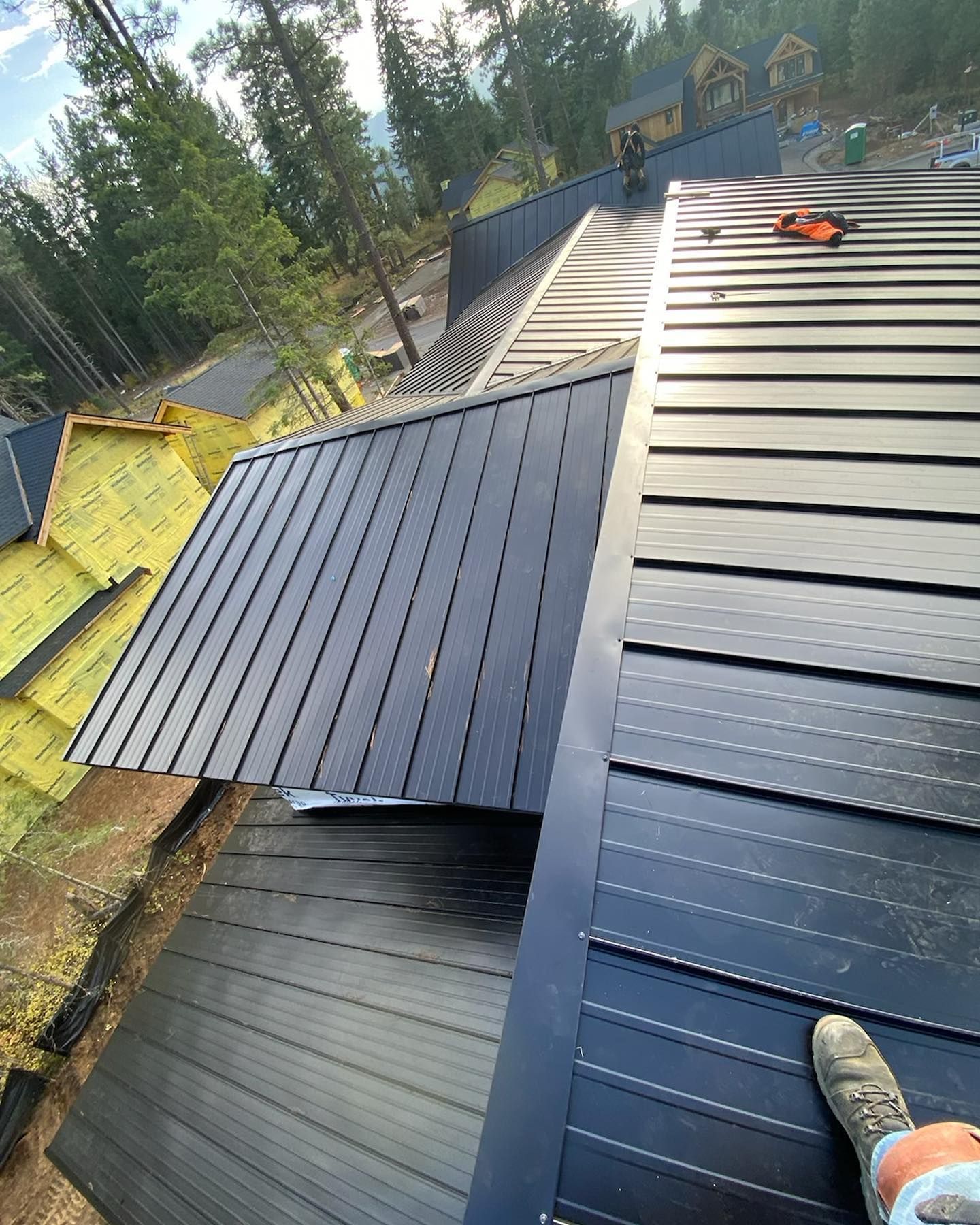 Construction worker on a dark metal roof, trees in the background, autumn colors.