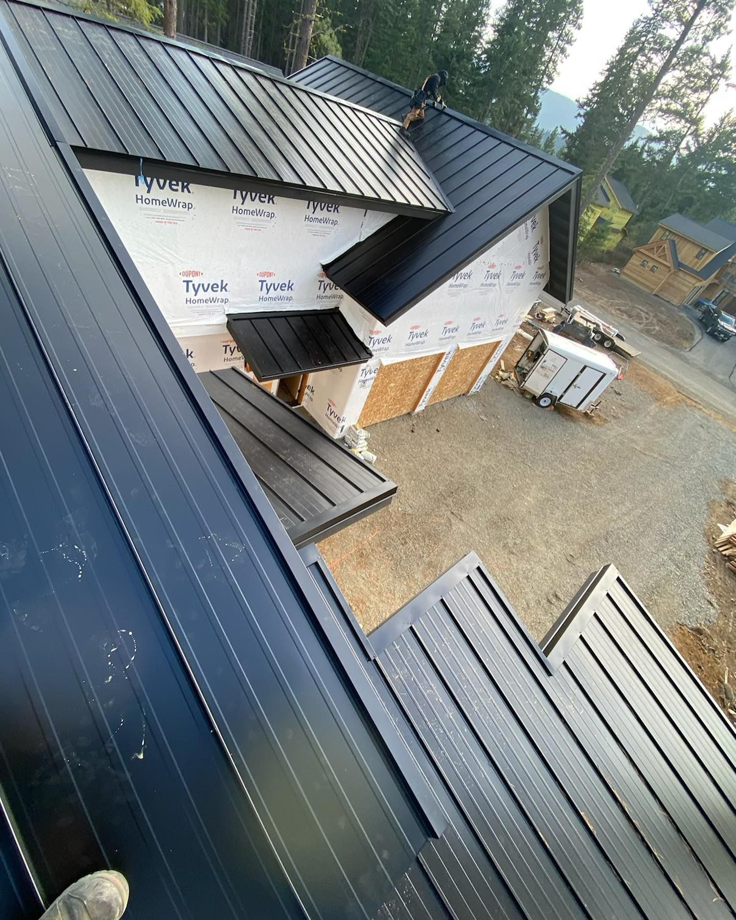 Black metal roof installation on a house under construction; Tyvek wrap visible.