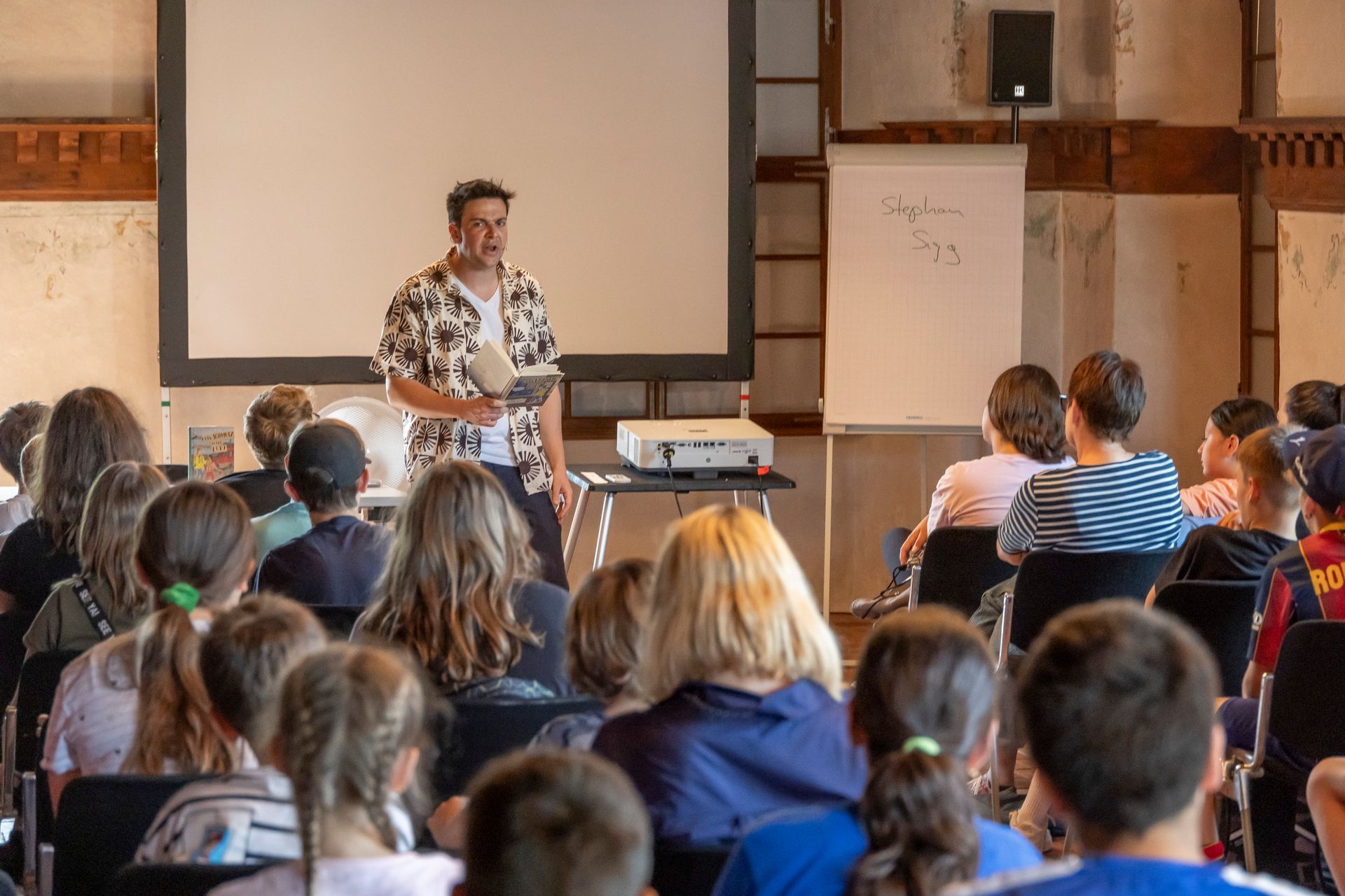 Ein Mann hält vor einer Gruppe von Kindern in einem Klassenzimmer einen Vortrag.