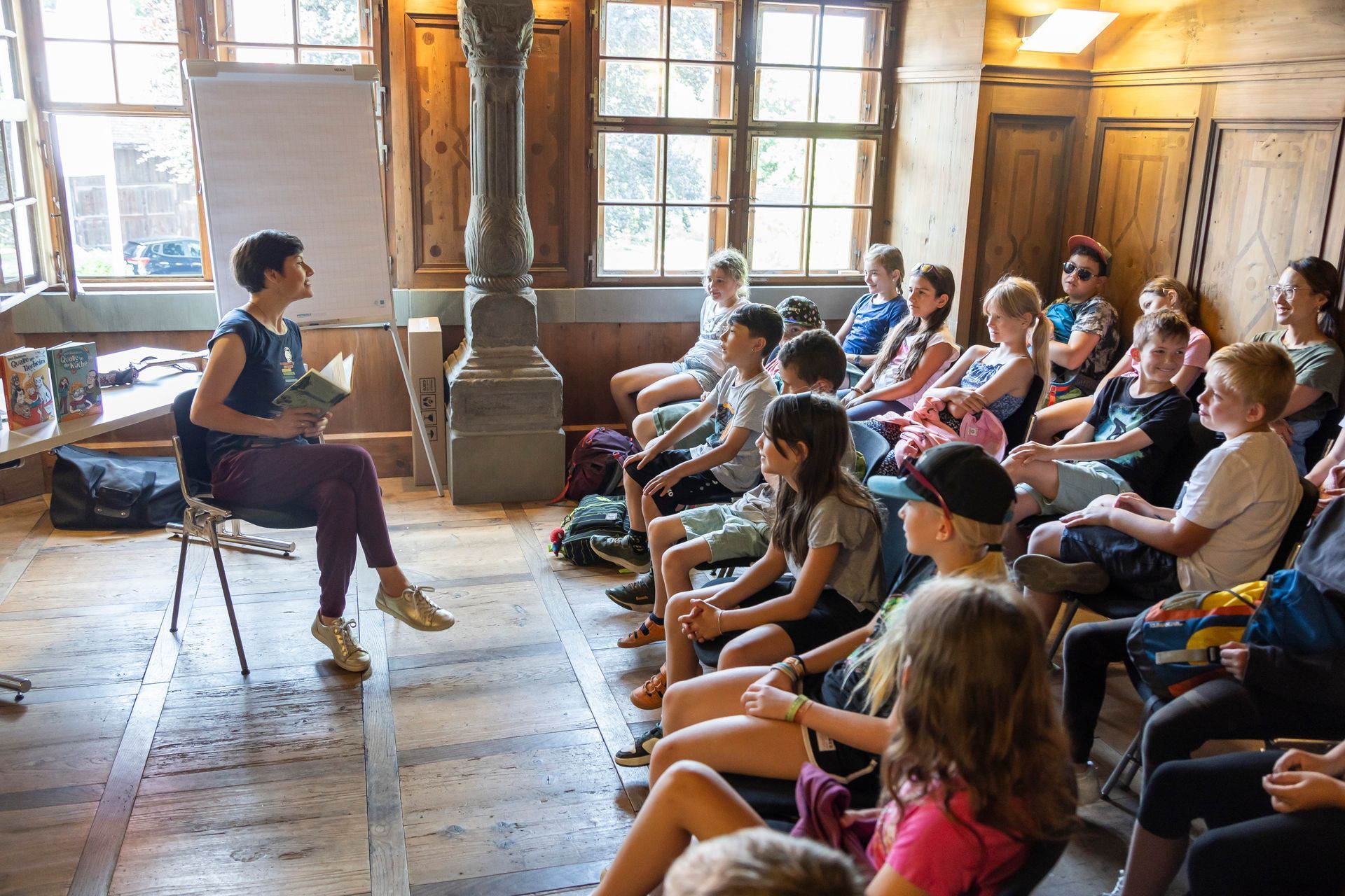 Eine Frau sitzt auf einem Stuhl und liest einer Gruppe von Kindern ein Buch vor.