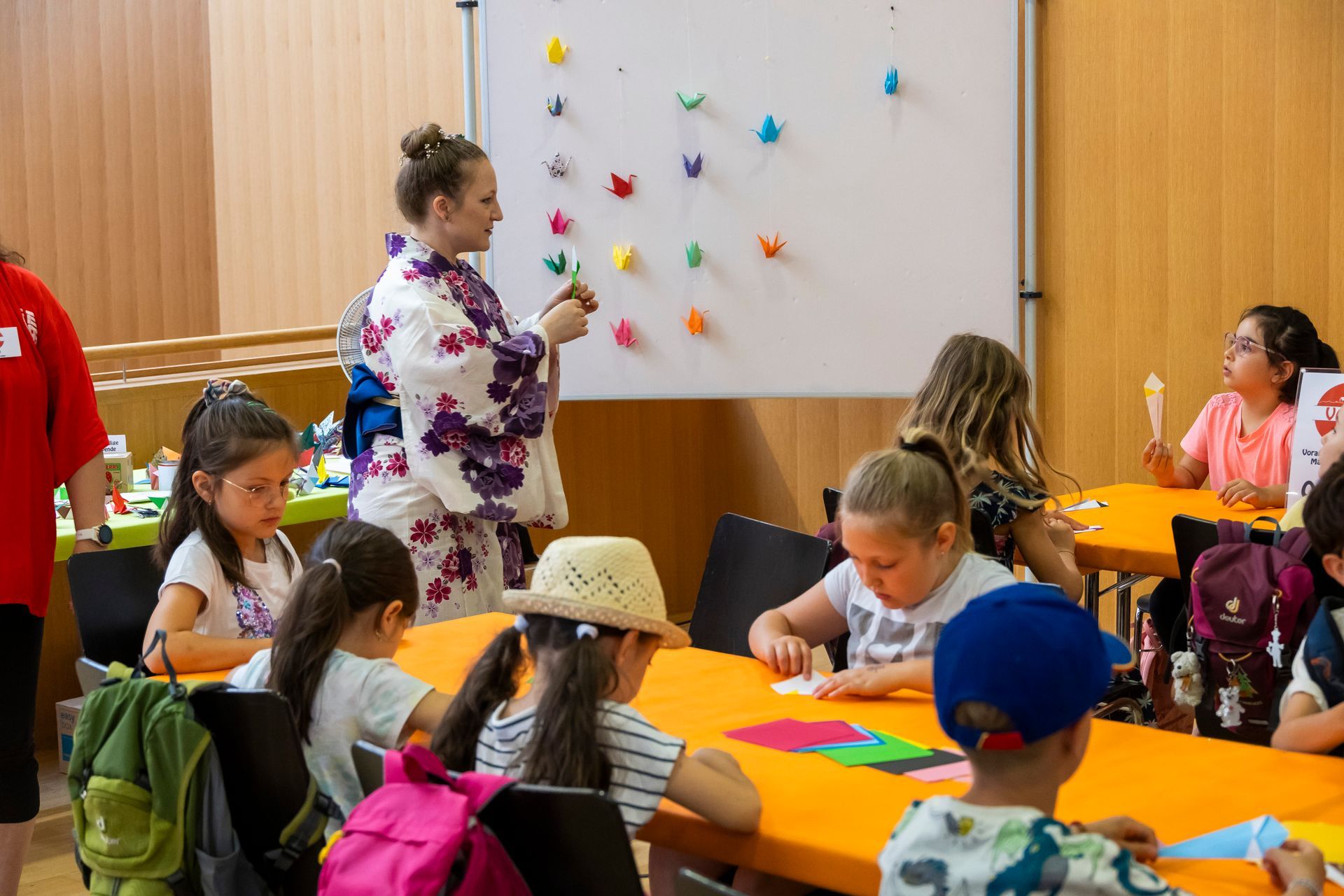 Eine Gruppe von Kindern sitzt an Tischen vor einer weißen Tafel.