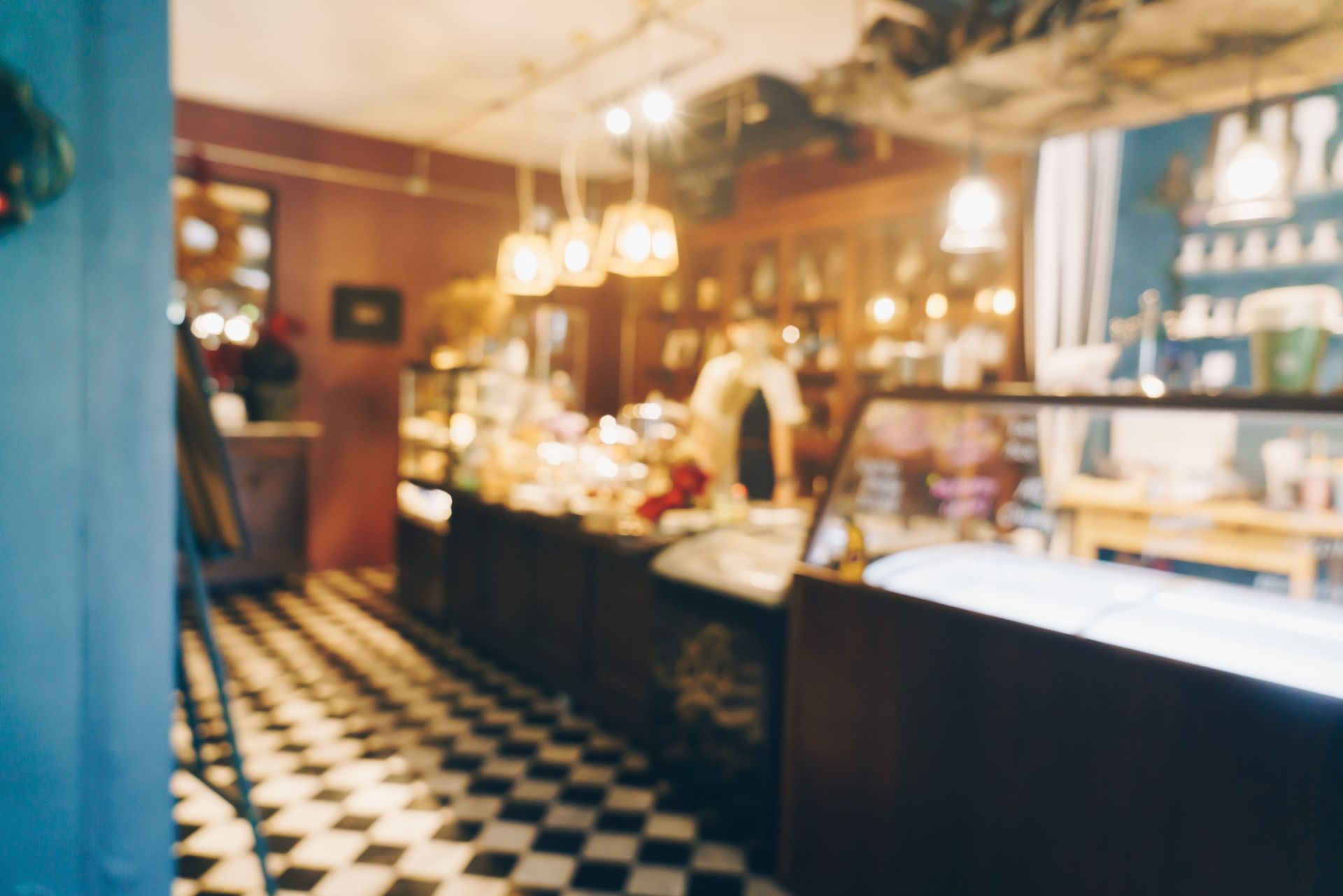 Warm cafe interior with checkered floor, pastry counter, and softly lit display shelves