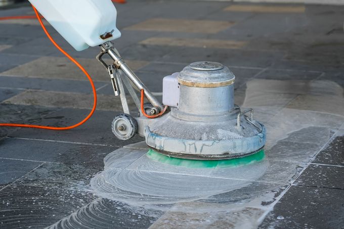 A person is cleaning a tiled floor with a machine.