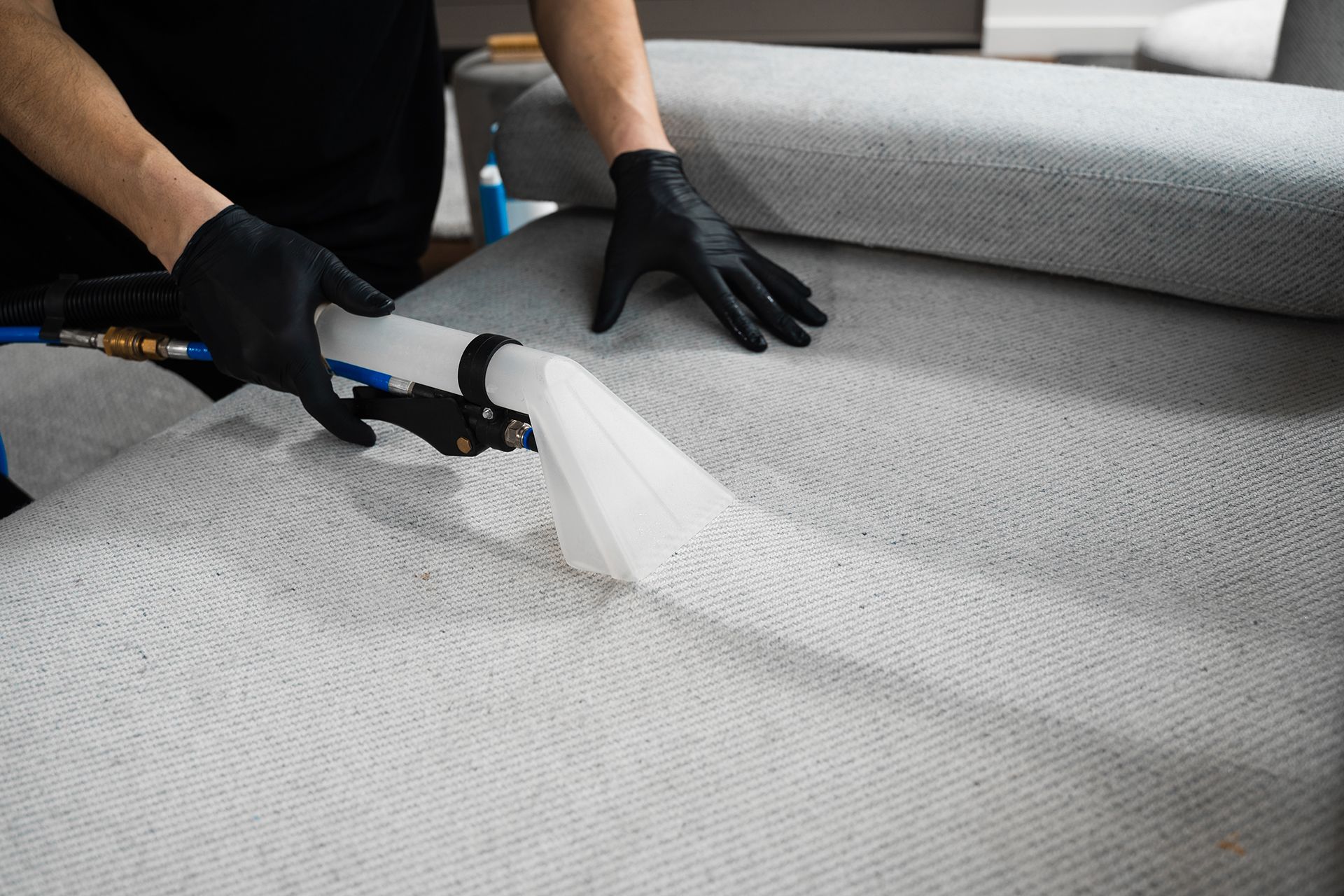 A person is cleaning a couch with a vacuum cleaner.