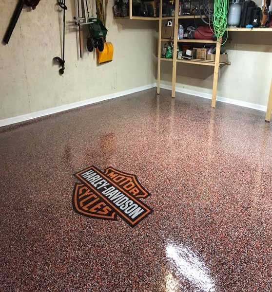 Garage with glossy speckled epoxy floor and Harley-Davidson logo near shelving and tools.