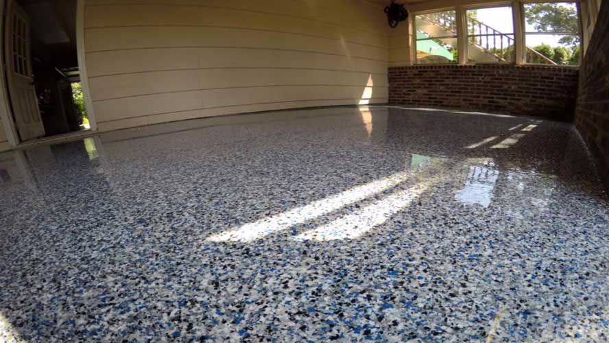 Speckled epoxy garage floor with sunlight reflections in an empty indoor space