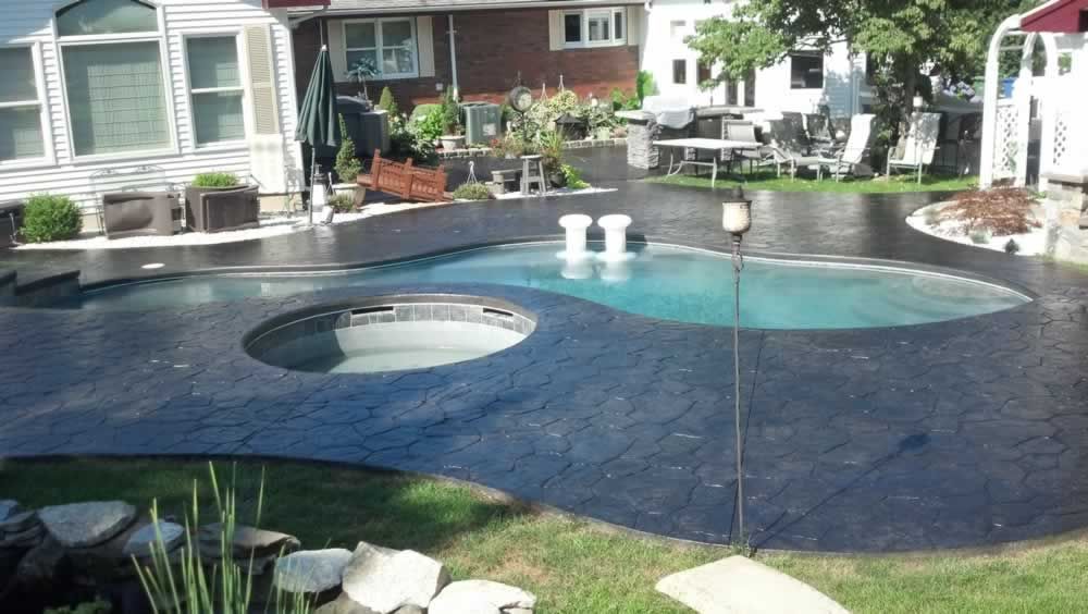Backyard pool with a circular spa, dark stone decking, and lounge chairs near a house