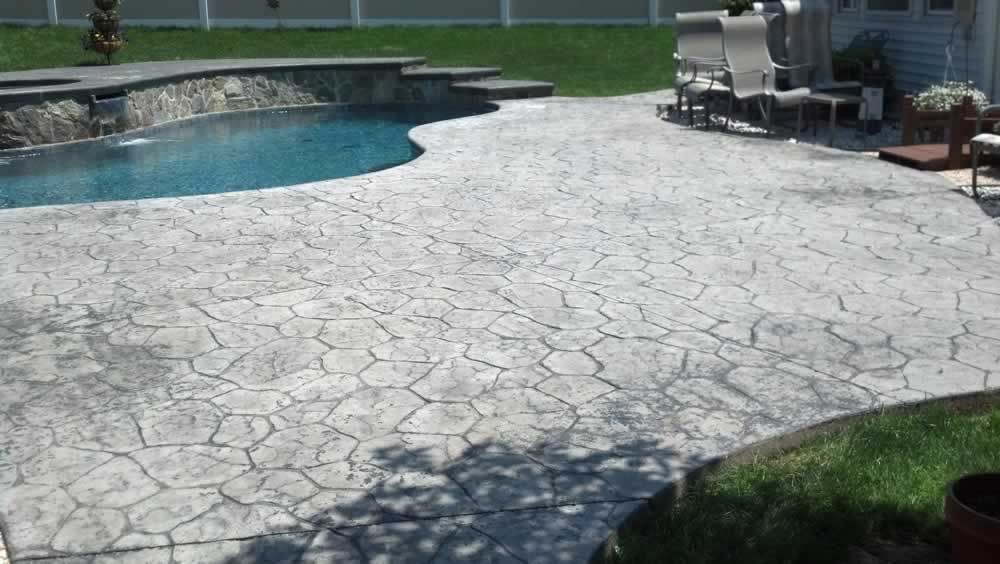 Backyard patio with stamped concrete deck, curved swimming pool, and lounge chairs