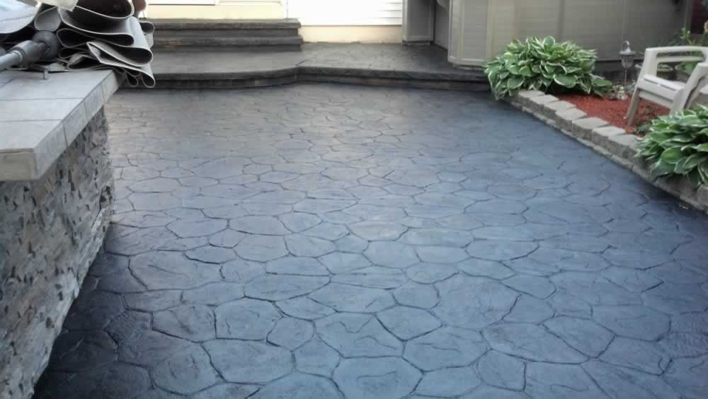 Stone-patterned driveway leading to a porch, with steps, potted plants, and a red flower bed along the edge.