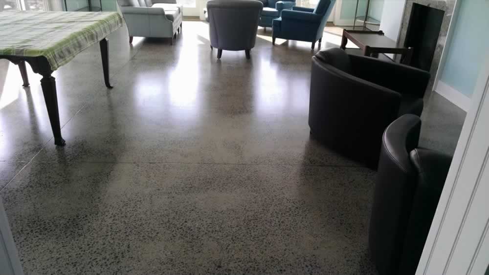 Indoor lounge with black chairs, a green table, and bright sunlight on polished concrete floor