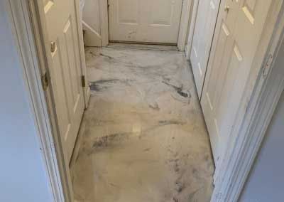 Damaged hallway floor with torn, stained carpet leading to a closed door