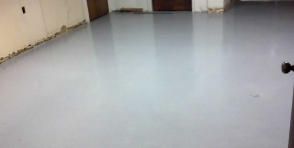 Empty room with a glossy light gray floor and white walls, viewed from a corner.
