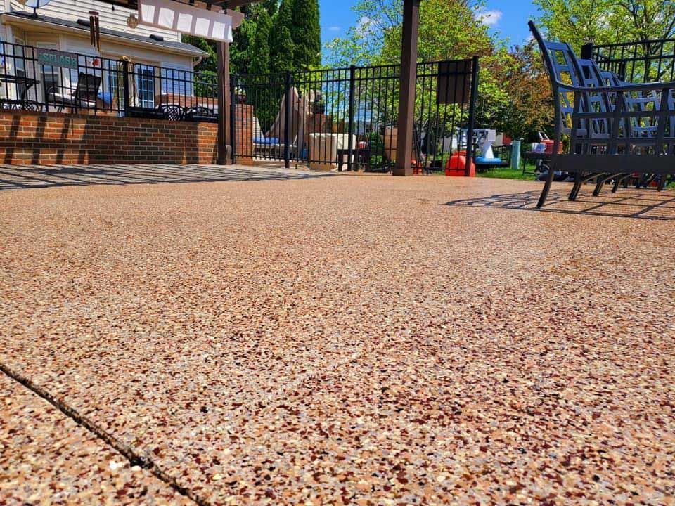 Low-angle view of a pebble-textured patio beside a fenced outdoor seating area and building.