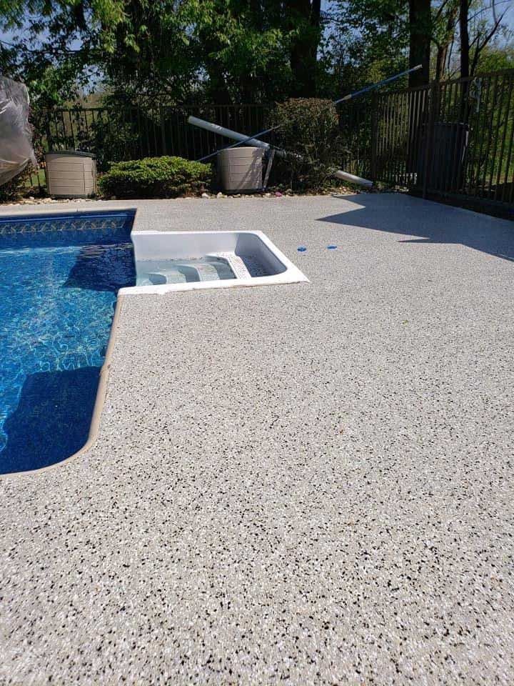 Poolside patio with blue pool, white textured deck, and black fence in bright sunlight