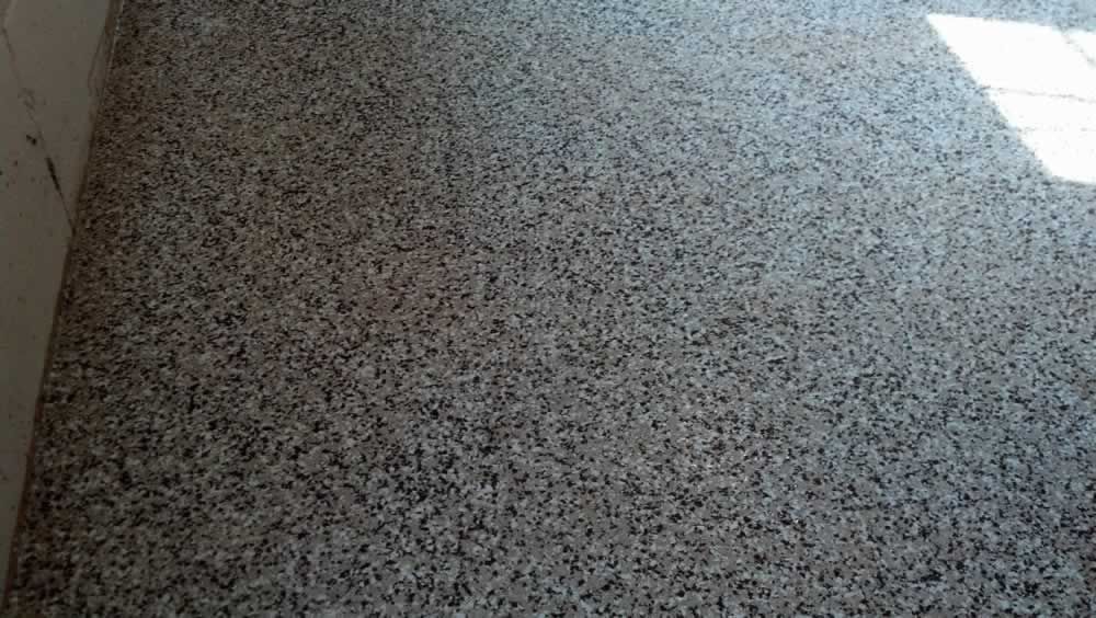 Speckled gray terrazzo floor beside a sunlit white wall corner