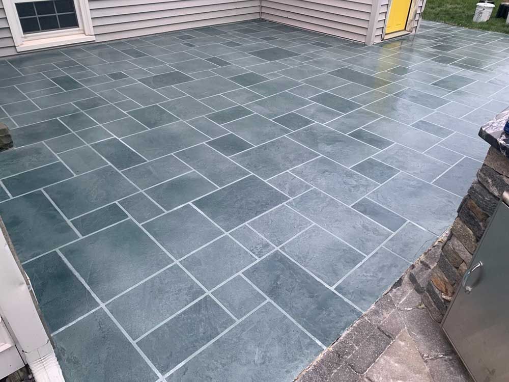 Wet slate patio tiles beside a house wall and steps, with a yellow door in the background