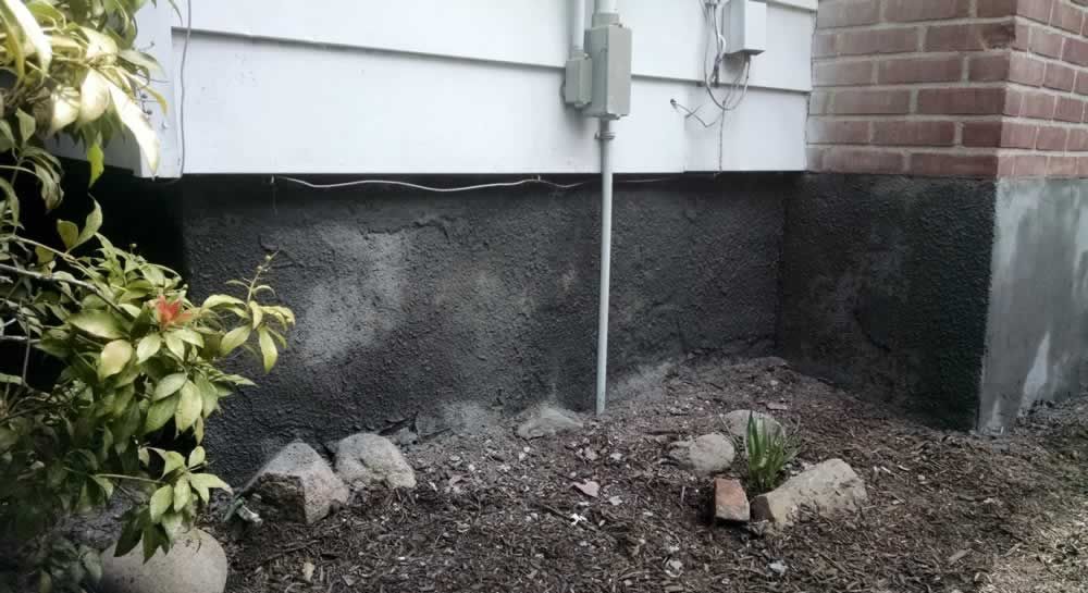 Side of a house with white siding, brick corner, utility meter, and gravel landscaping with rocks and a small plant