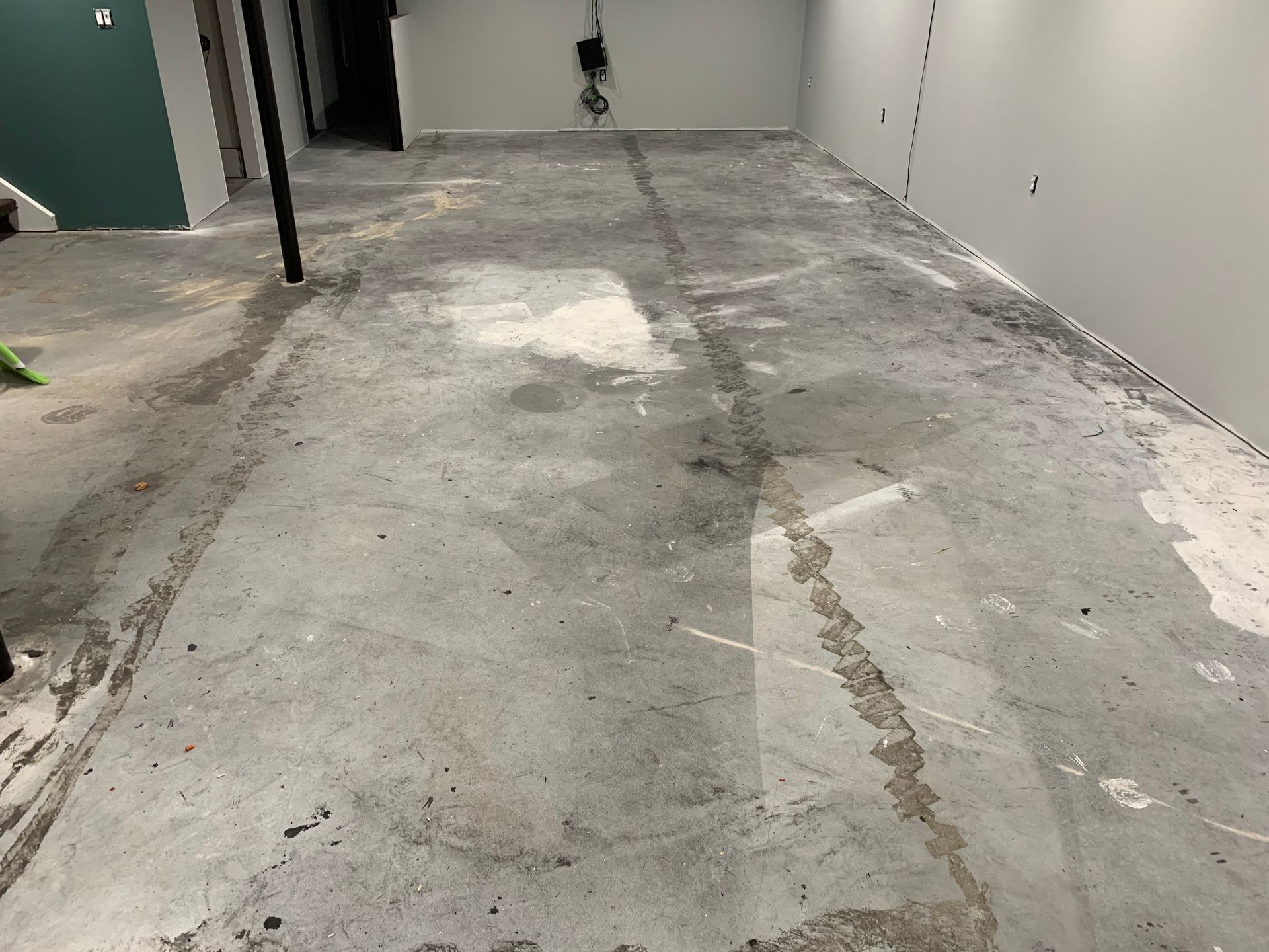Rough concrete floor in an unfinished room with patched cracks and white walls