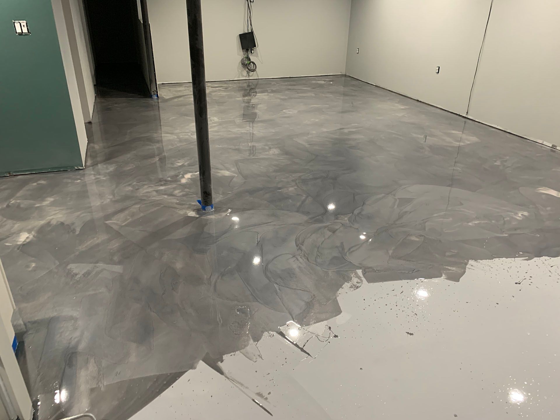 Wet gray concrete floor in an empty room, with a central support pole and reflections from overhead lights.