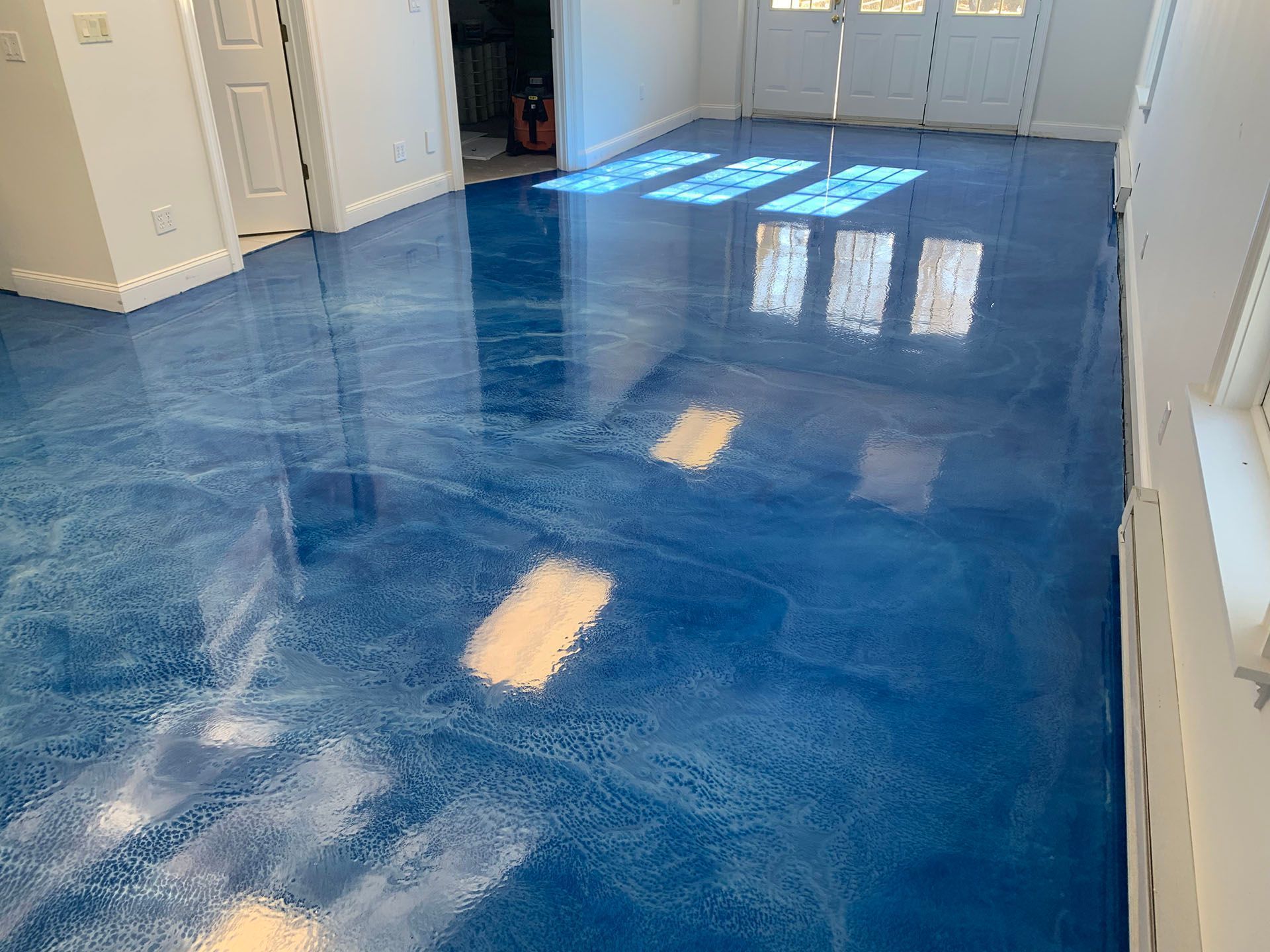 Blue epoxy floor in a bright empty room with white walls and doors, reflecting light from windows