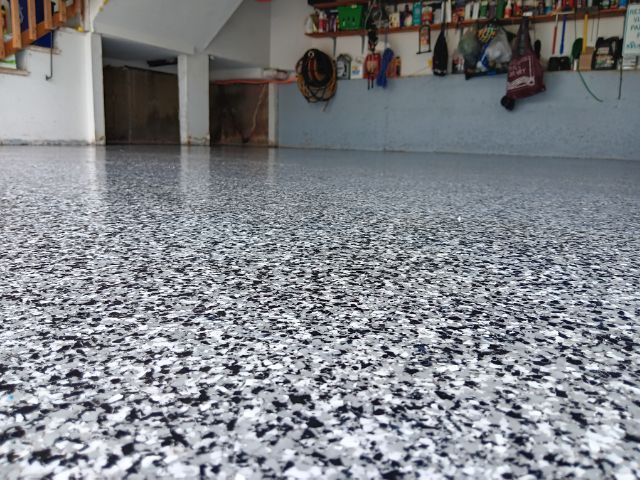 Speckled epoxy floor in an indoor garage or workshop with tools and items hanging on the wall.